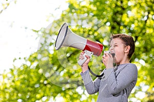 Announcing concept, boy shouting or screaming through the megaphone over forest background with copyspace