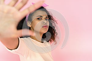 Annoyed african girl look at camera show stop hand gesture on pink background
