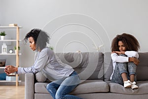 Annoyed african single mother and upset daughter sit on sofa