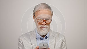 Annoyed aged man using phone in studio. Focused guy putting on glasses indoors.