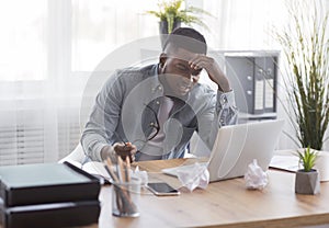 Annoyed black employee looking at laptop screen with despair