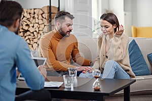 Annoyed caucasian couple of man and woman having conversation with psychologist on therapy session in light room.