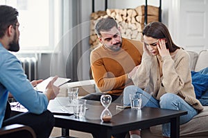 Annoyed caucasian couple of man and woman having conversation with psychologist on therapy session in light room.