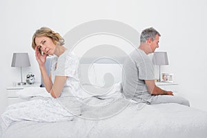 Annoyed couple sitting on different sides of bed having a dispute