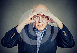 Annoyed elderly man looking through hands like binoculars has vision problems