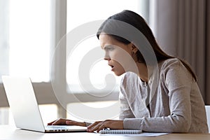 Annoyed female sitting at desk looking on laptop screen