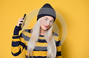 Annoyed girl on the phone, model wearing woolen cap and sweater, isolated on yellow background. Annoying woman talking. Nuisance