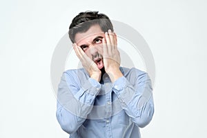 Annoyed guy with bristle, leaning face on hand and looking indifferent at camera