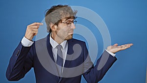 Annoyed yet handsome young man in business suit, showing room for ad on his palm, pointing to forehead and looking bothered. over