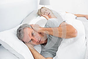 Annoyed man blocking his ears from noise of wife snoring