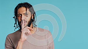 Annoyed man doing shushing hand gesturing, irritated by noise, studio background