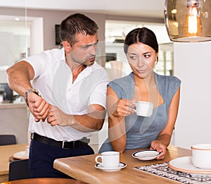 Annoyed man pointing at wristwatch to girlfriend drinking tea