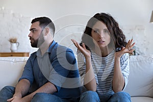 Annoyed married couple sitting on couch apart, after conflict,