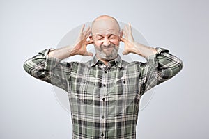 Annoyed mature man plugging ears with fingers
