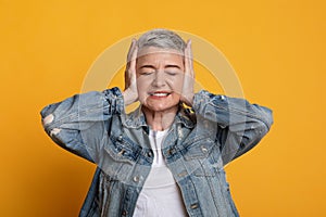 Annoyed Middle Aged Woman Covering Ears In Stress, Standing Over Yellow Background