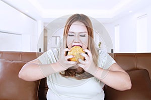 Annoyed obese woman eating a hamburger