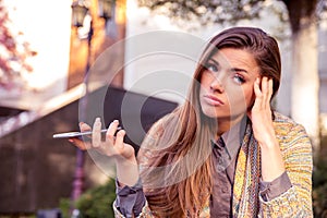 Annoyed sad woman with mobile phone standing outside in the street with an urban background
