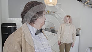 Annoyed senior man looking back at blurred woman gesturing at the background and shaking head. Portrait of angry mature