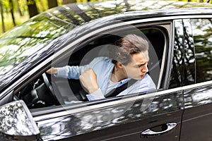 Annoyed tired young man is riding driving car. Businessman is late for meeting. Driver brunette in grey suit stuck in traffic jam