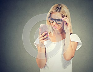 Annoyed upset woman in glasses looking at her cell phone with frustration