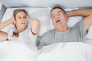 Annoyed wife blocking her ears from noise of husband snoring