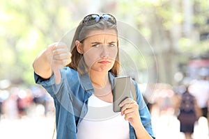 Annoyed woman holding a smart phone with thumbs down