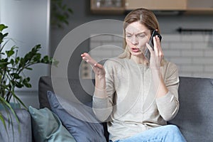 Annoyed woman at home sitting on the couch and talking on the phone