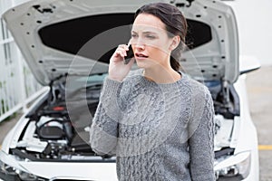 Annoyed woman on the phone beside her broken down car