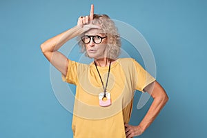 Annoyed woman, showing loser sign standing with disrespectful expression