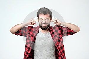 Annoyed young man plugging ears with hands. Studio shoot