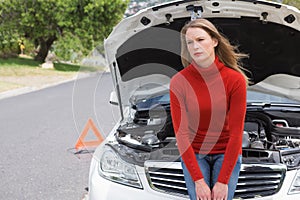 Annoyed young woman beside her broken down car