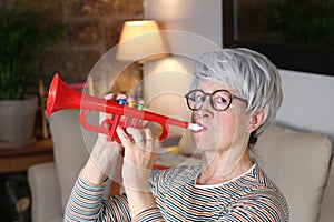 Annoying senior woman playing plastic trumpet