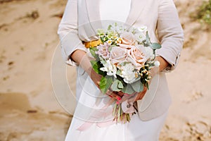 Anonymous bride with wedding bouquet close up at sandy beach.