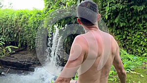 Anonymous brunet man standing near waterfall enjoying view in tropical paradise. Vacation in wild jungle to explore