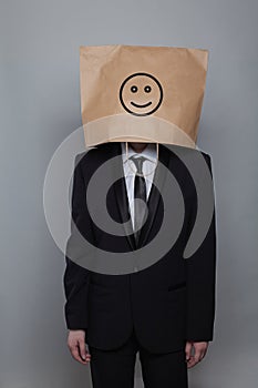 Anonymous businessman hiding his head behind happy smile emoticon on gray background