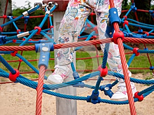 Anonymous child, active elementary school age girl climbing, walking on ropes legs closeup, playground, healthy outdoor activities
