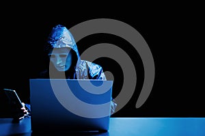 Anonymous computer hacker in white mask and hoodie. Obscured dark face attacking people through a smartphone.