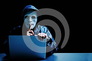 Anonymous computer hacker in white mask and hoodie. Obscured dark face making silence gesture on dark background, Data thief,