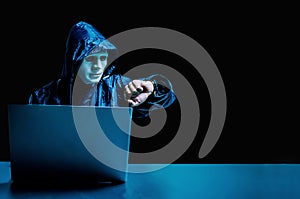 Anonymous computer hacker in white mask and hoodie. Obscured dark face using laptop computer for cyber attack and checking time ,