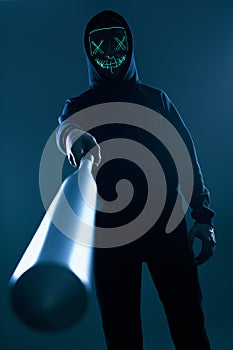 Anonymous criminal man with baseball bat in a black hoodie and neon mask