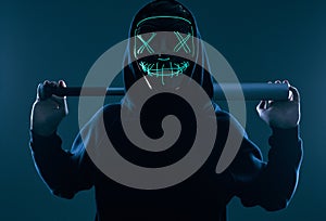 Anonymous criminal man with baseball bat in a black hoodie and neon mask