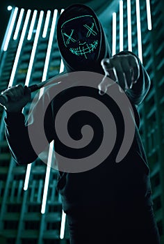 Anonymous criminal man with baseball bat in a black hoodie and neon mask