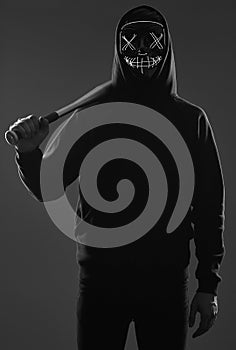 Anonymous criminal man with baseball bat in a black hoodie and neon mask