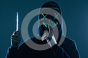 Anonymous criminal man with kitchen knife in a black hoodie and neon mask