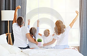 Anonymous family mother, father and children  wake up in   morning and   stretch up by looking out the window in bed   at home