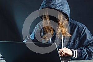 Anonymous girl hacker uses a laptop to hack system. Stealing personal data. Creation and infection of malicious virus.