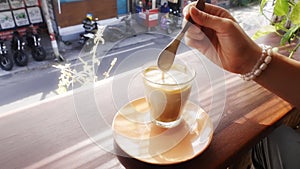 Anonymous girl stirring thick milk foam of a coffee drink on a window sill of a cafe overlooking a Balinese street