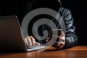Anonymous hacker in dark hoodie working on laptop at night. Cybercrime and internet security threat concept. Mysterious