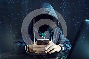 An anonymous hacker without a face uses a mobile phone to hack the system. The concept of cyber crime