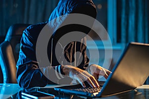 Anonymous hacker programmer uses a laptop to hack the system in the dark. Concept of cybercrime and hacking database